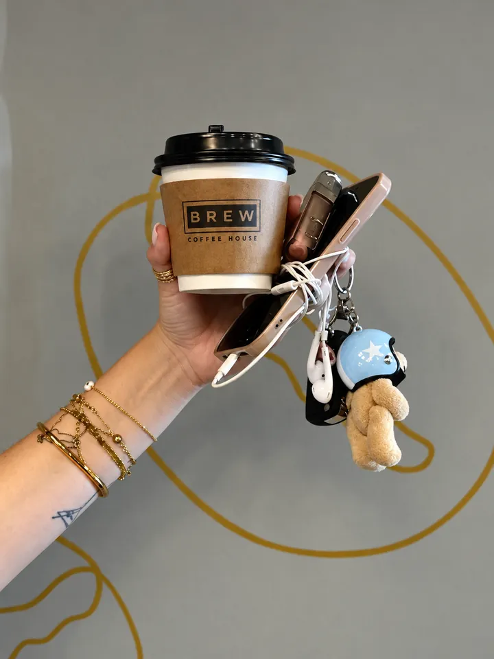 A Brew Coffee House cup held up with a phone and keys